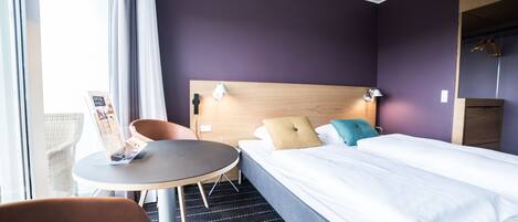 A hotel room with a bed, a round table, a chair, and a window with curtains.