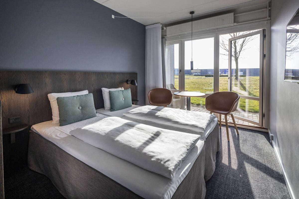 A hotel room with a large bed, two bedside tables, a chair, and a view of the outdoors.