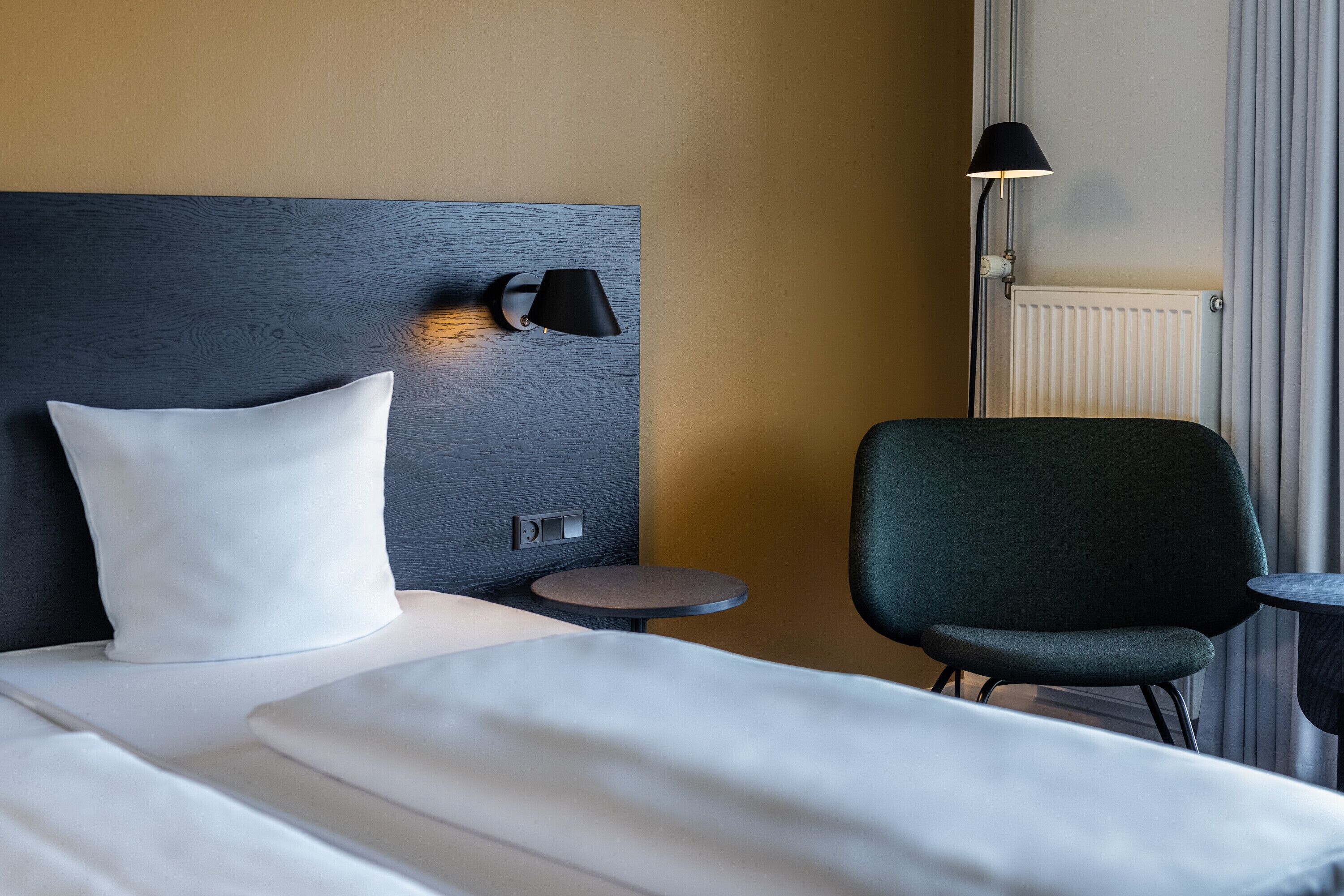 Una habitación de hotel con una cama, una silla, una mesita y una lámpara.