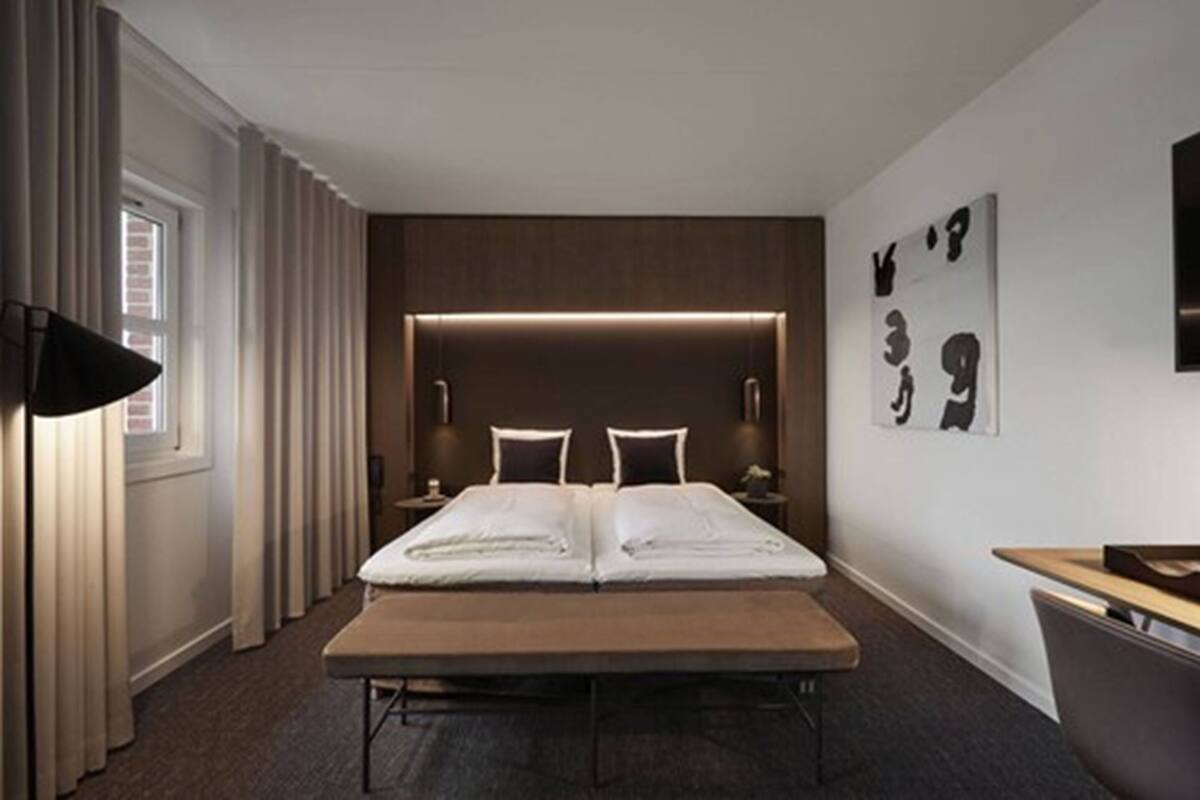 A hotel room with a double bed, bedside tables, a desk, and a large window with curtains.