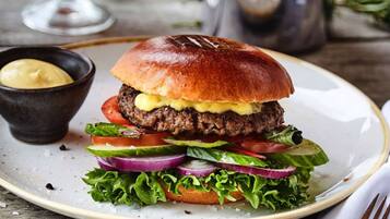 A burger with lettuce, tomato, and red onion on a plate, accompanied by fries and a small bowl of sauce.