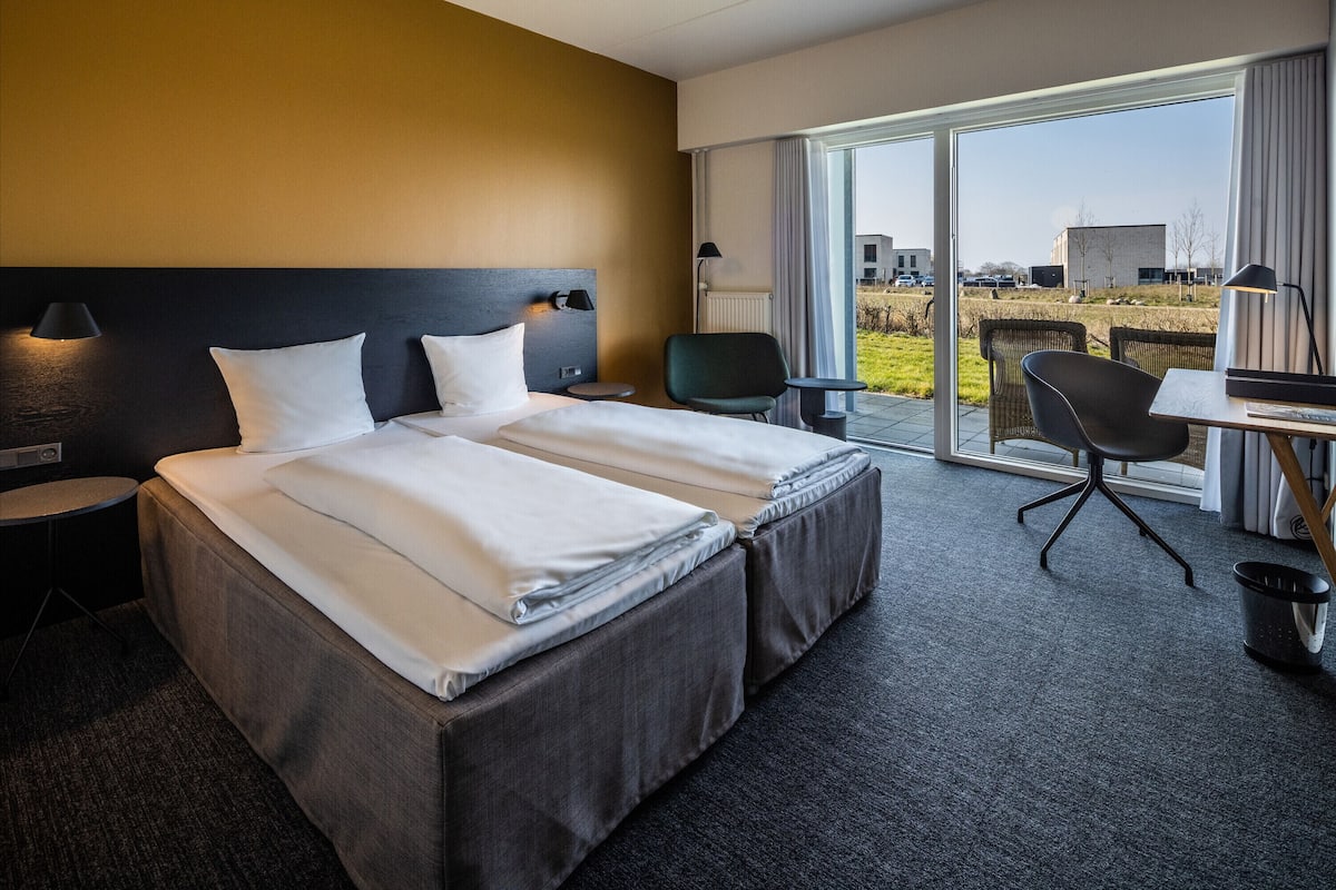 A hotel room with a large bed, a desk with a chair, and a view of the outside.