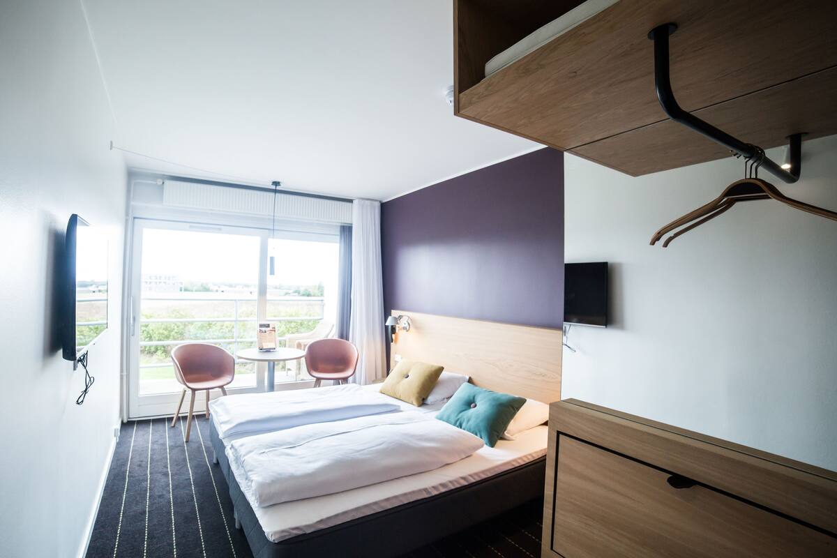 A hotel room with a bed, a desk, a chair, a TV, and a window with a view.