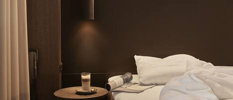 Ein Hotelzimmer mit einem ordentlich bezogenen Bett, einem Nachttisch mit einem Glas Wasser und einer hängenden Pendelleuchte.
