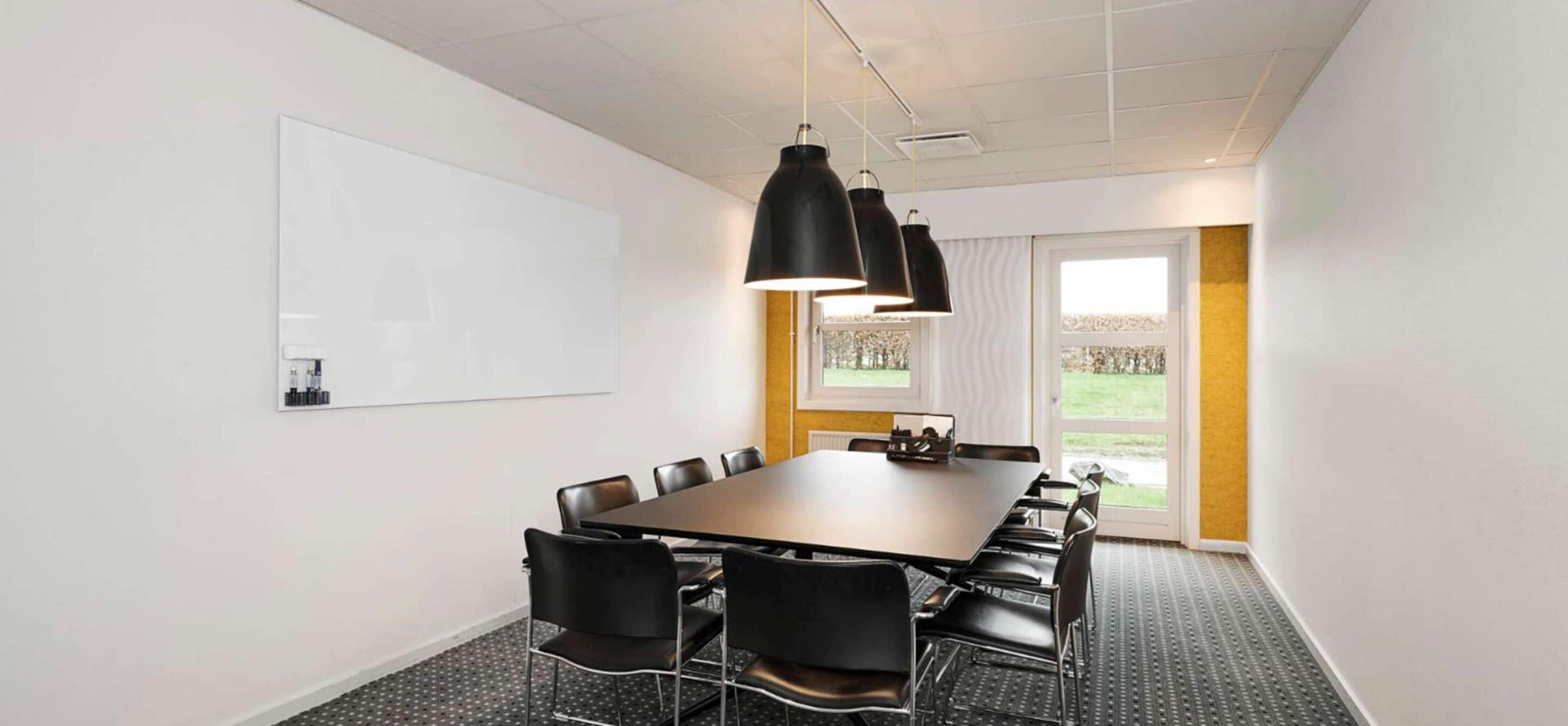 A conference room with a large table, black chairs, a whiteboard, and pendant lights.