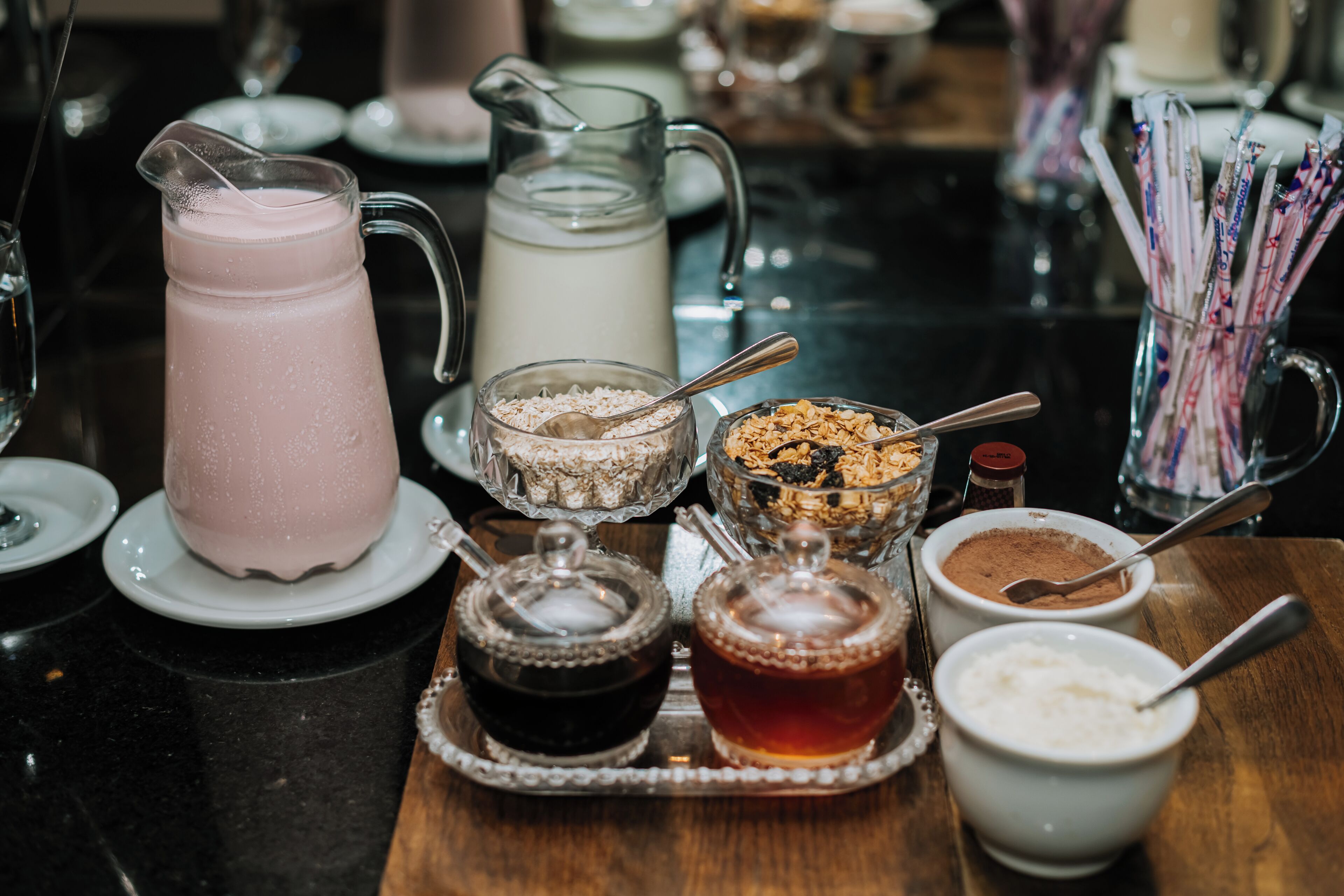 Una mesa con una jarra de bebida rosa, una jarra de leche, tazones de cereal y diferentes condimentos.