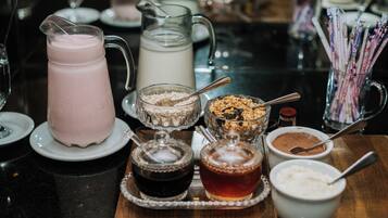 Una mesa con una jarra de bebida rosa, una jarra de leche, tazones de cereal y diferentes condimentos.