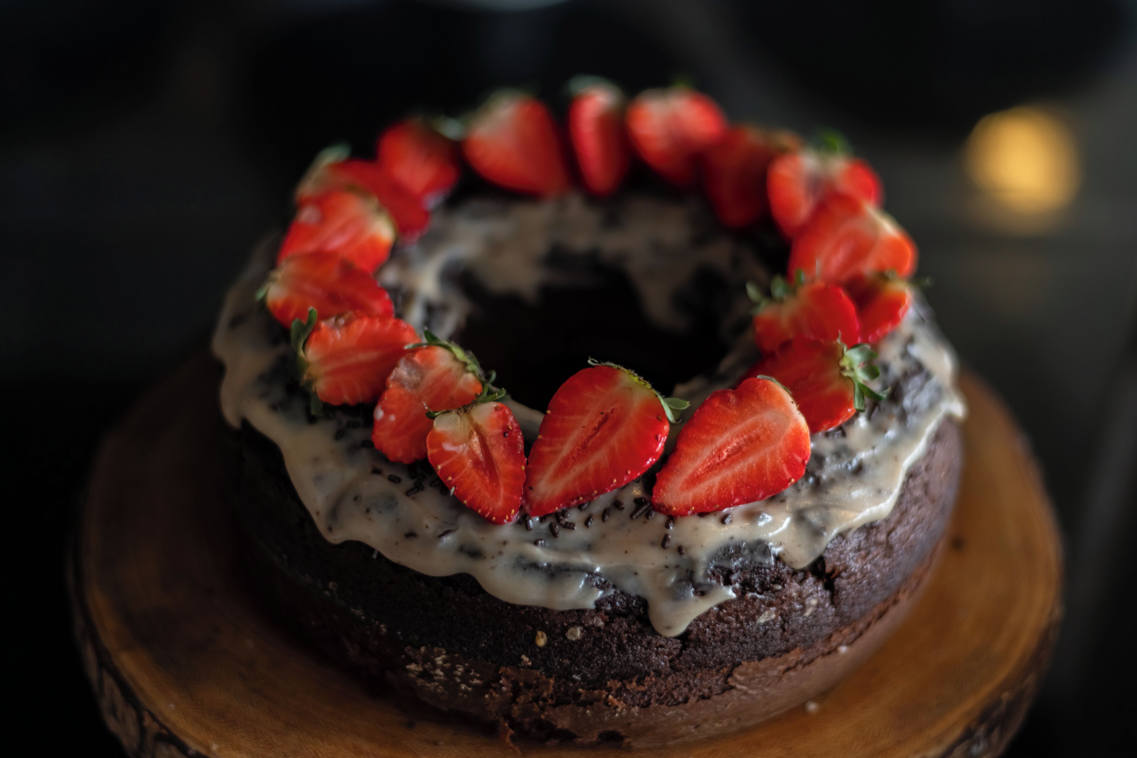 Una torta al cioccolato con fragole sopra, su un tagliere di legno.