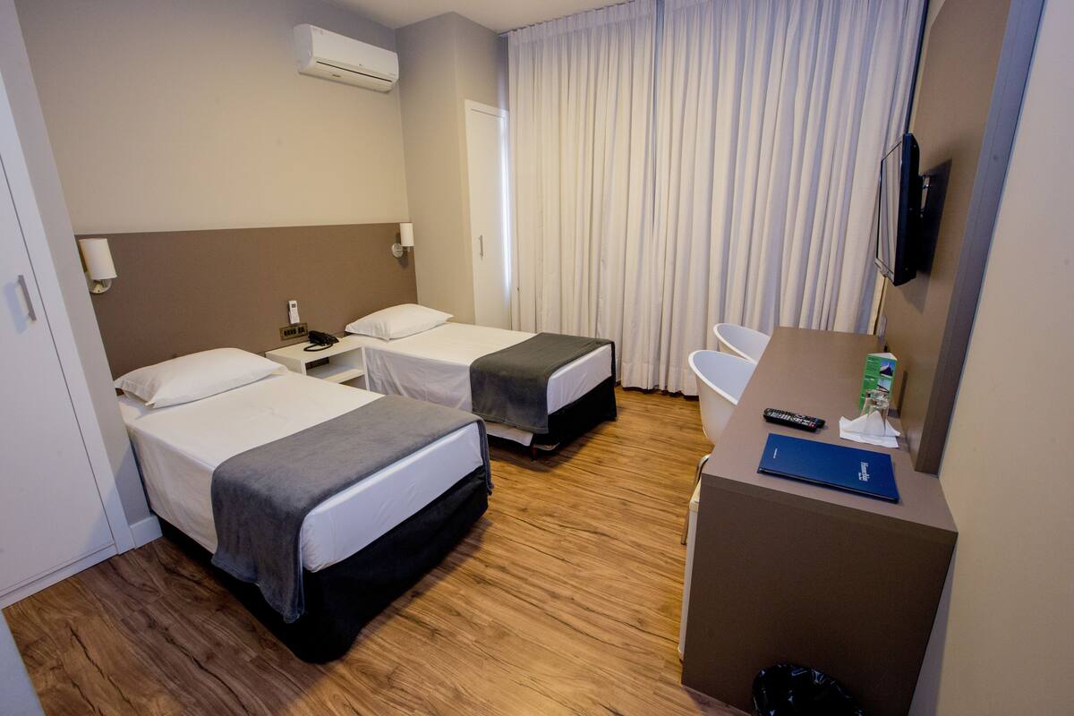 Habitación de hotel con dos camas, un escritorio, una silla, un televisor y una ventana con cortinas.