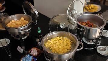 A buffet with various dishes including scrambled eggs, a dish labeled "Ovo Mexido," and a plate of bananas.