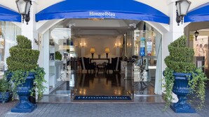 The entrance of Himmelblau Palace Hotel with a blue awning, a reception desk, and two potted plants. - Hotel Himmelblau (Blumenau)