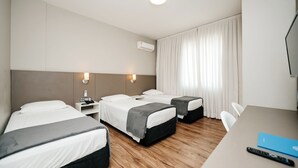 A hotel room with two beds, a desk, a chair, and an air conditioning unit. - Hotel Himmelblau (Blumenau)