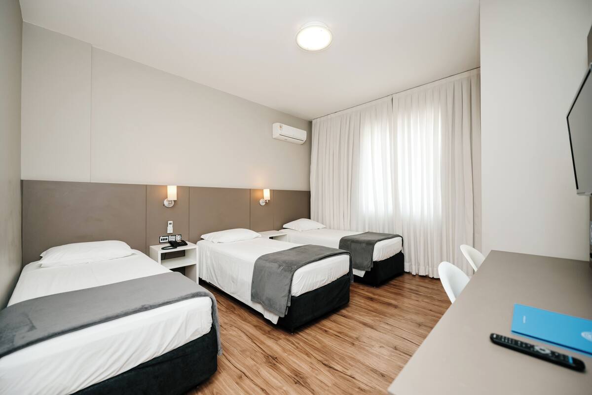 Habitación de hotel con dos camas, un escritorio, una silla y aire acondicionado.