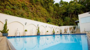 A swimming pool with a tiled edge, surrounded by white walls with arched niches, each containing a statue and a potted plant. - Hotel Himmelblau (Blumenau)