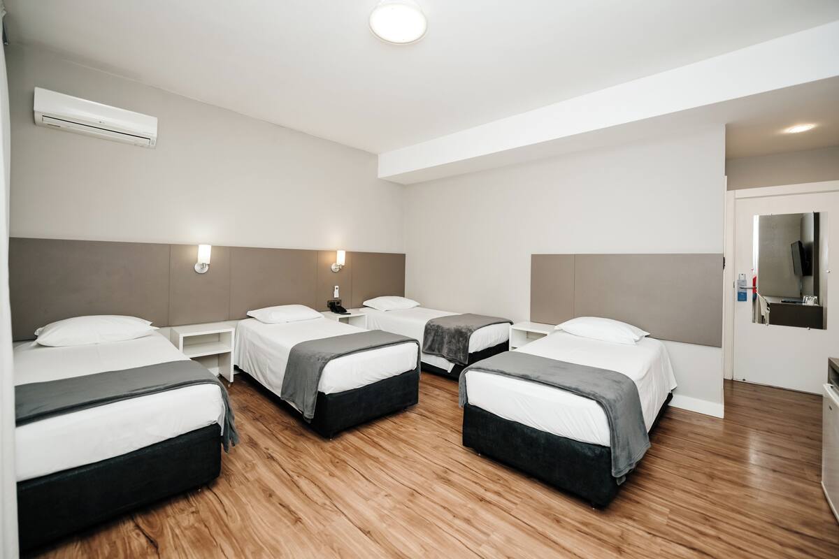 Habitación de hotel con cuatro camas individuales, suelo de madera, unidad de aire acondicionado integrada y un pequeño escritorio con teléfono.
