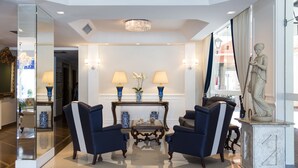 A lobby with two armchairs, a coffee table, and a statue. There are lamps on the wall and a chandelier. - Hotel Himmelblau (Blumenau)