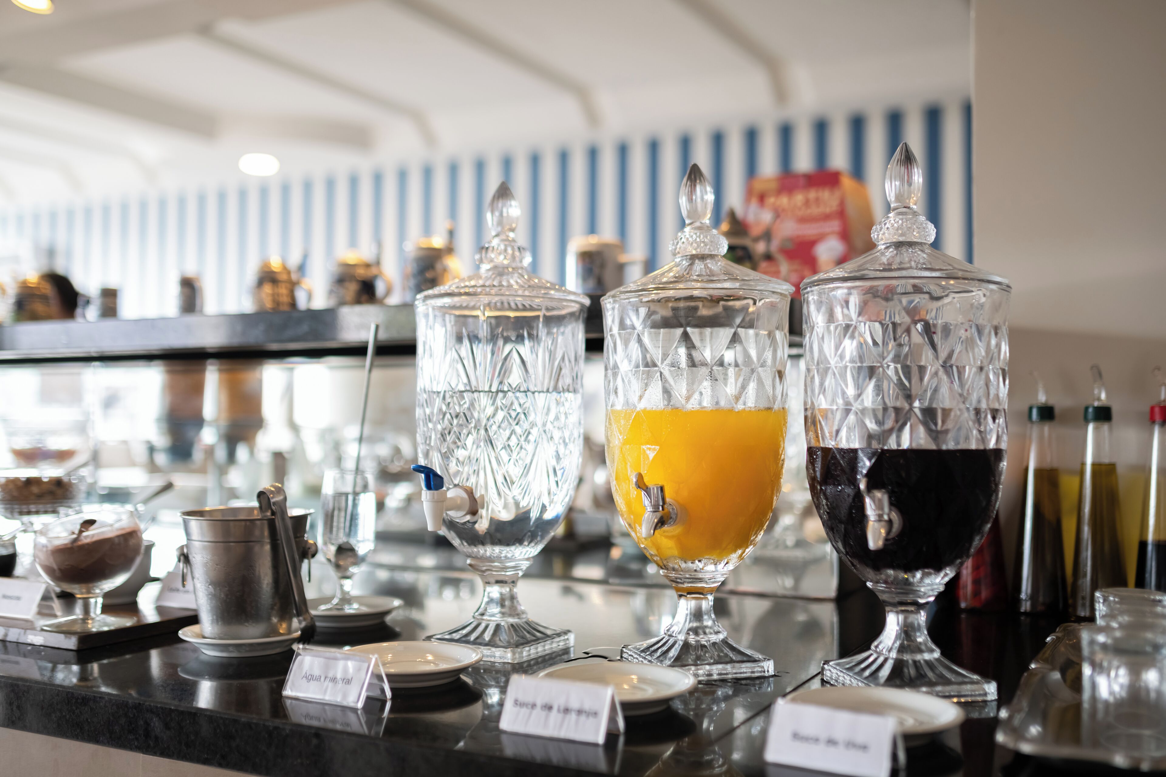 A bar area with various drink dispensers and containers, including a water dispenser and two glass carafes, one with orange juice and the other with a dark beverage.