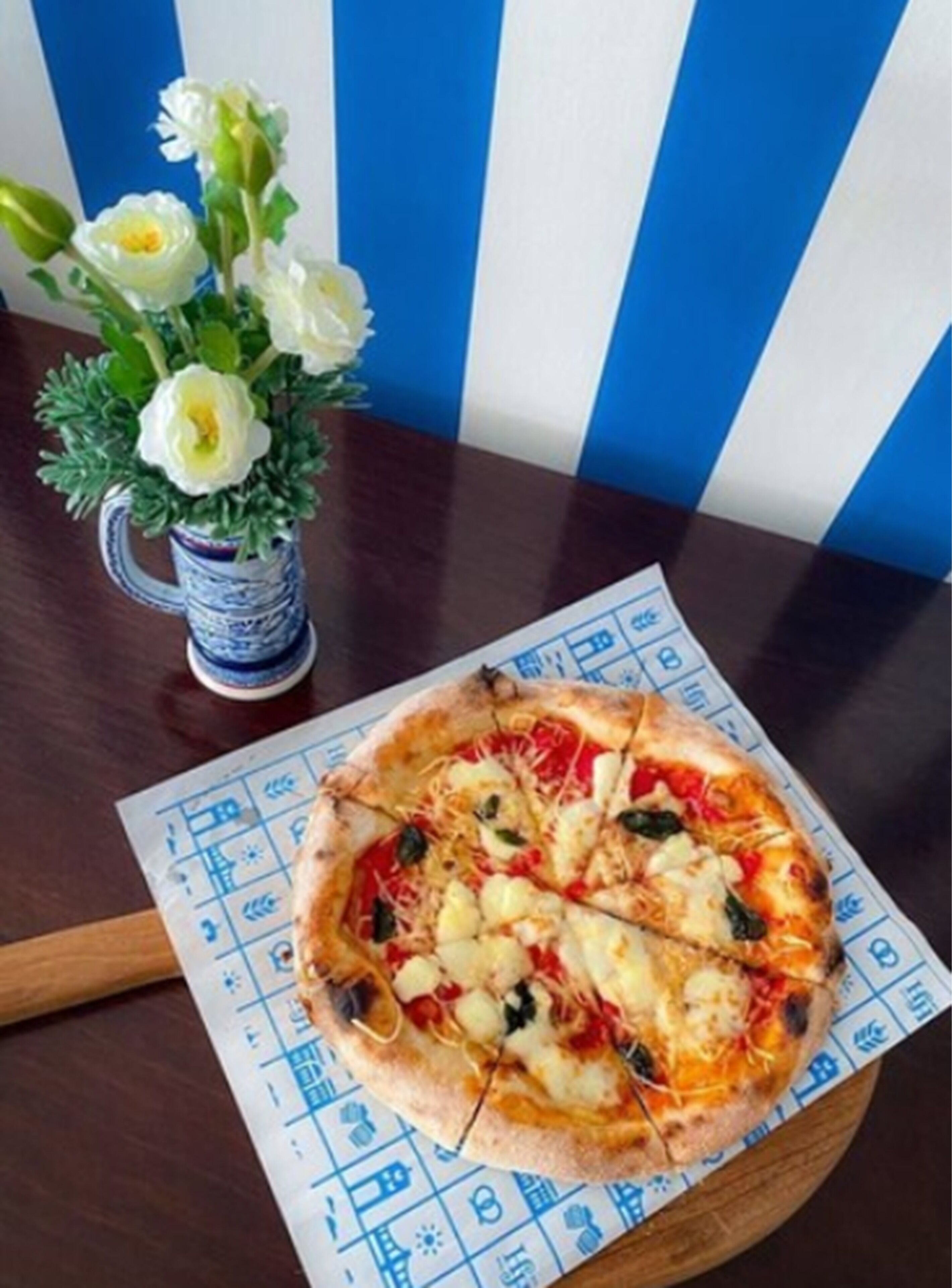 A pizza on a wooden board with a blue and white patterned tablecloth.
