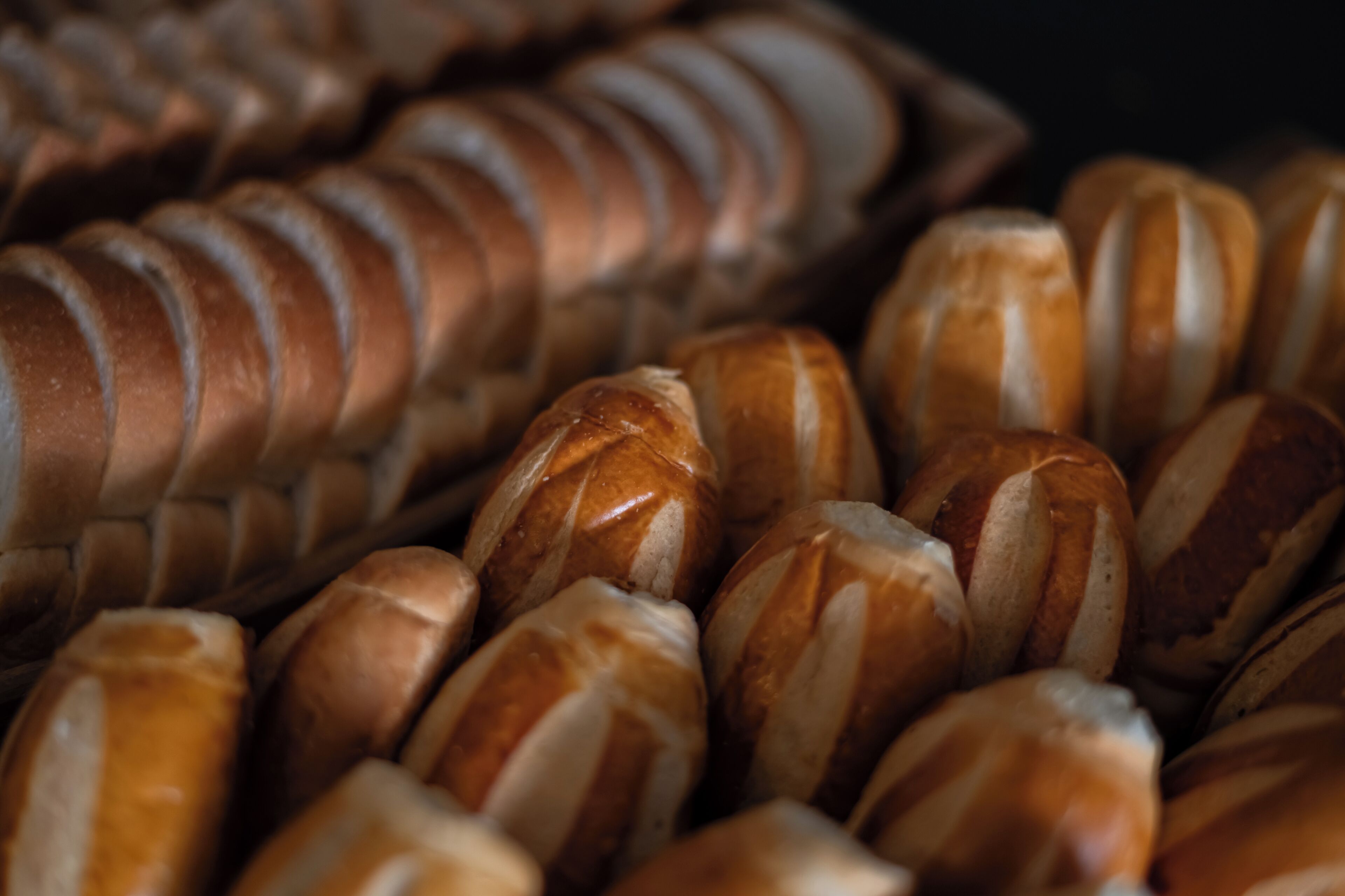 Primer plano de diferentes tipos de pan, incluyendo baguettes y bollos, con cortes visibles y una corteza dorada.