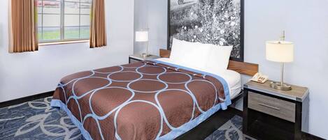 A hotel room with a bed, a nightstand, a lamp, a window with curtains, and a large wall-mounted picture.