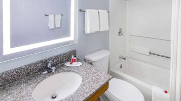 A bathroom with a granite countertop sink, a white toilet, a shower, and two white towels on towel racks.