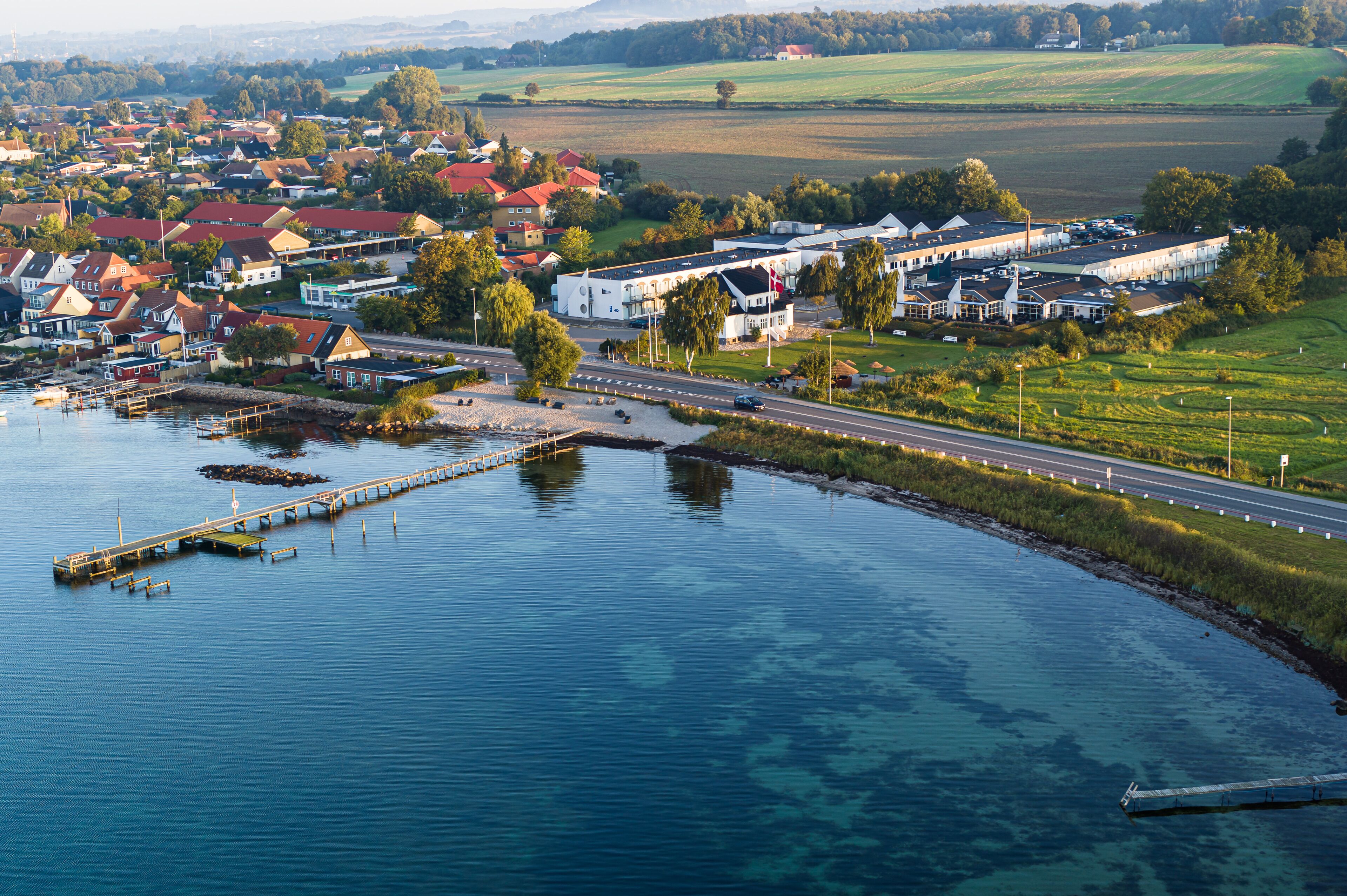 A coastal town with a marina, a bridge, and a road leading to a large white building with multiple windows.