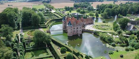 A castle with a moat, surrounded by manicured gardens and a large body of water.