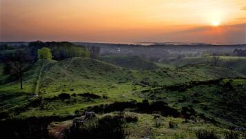 Paisaje con colinas ondulantes y una vista distante de un cuerpo de agua al atardecer.