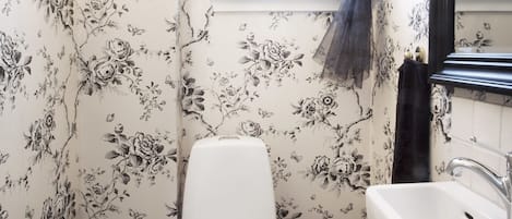 A bathroom with floral wallpaper, a white toilet, a sink, and a chandelier.