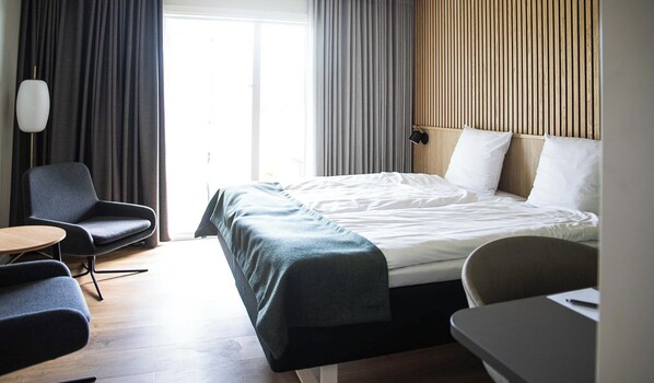 A hotel room with a bed, a desk, a chair, and a lamp.