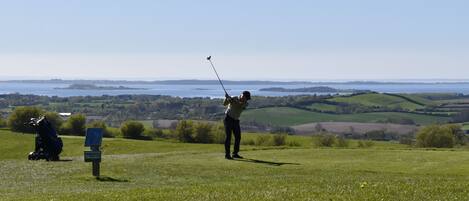 A golf course with a clear view of the water and distant hills.