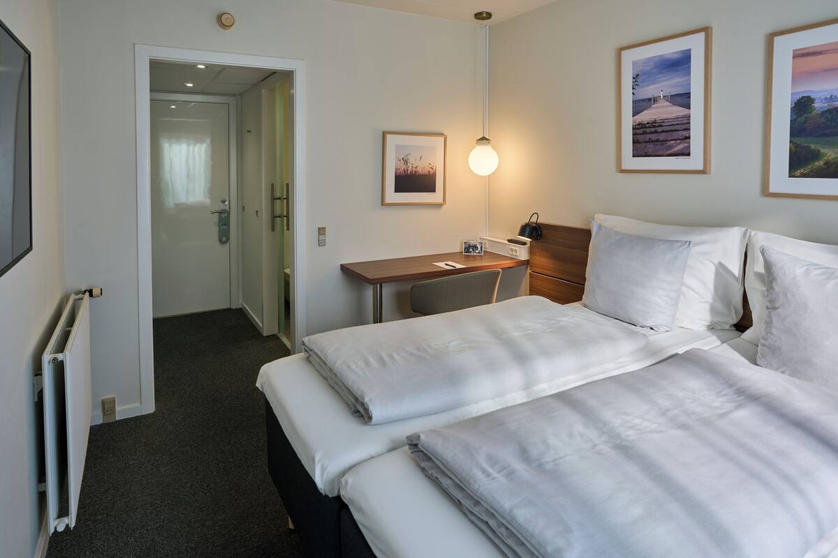 A hotel room with a bed, a desk, a chair, a lamp, and a framed picture on the wall.