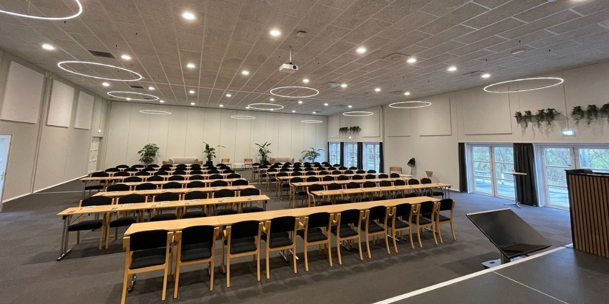 Ein Konferenzraum mit Tischen, Stühlen, einem Projektor und großen Fenstern.