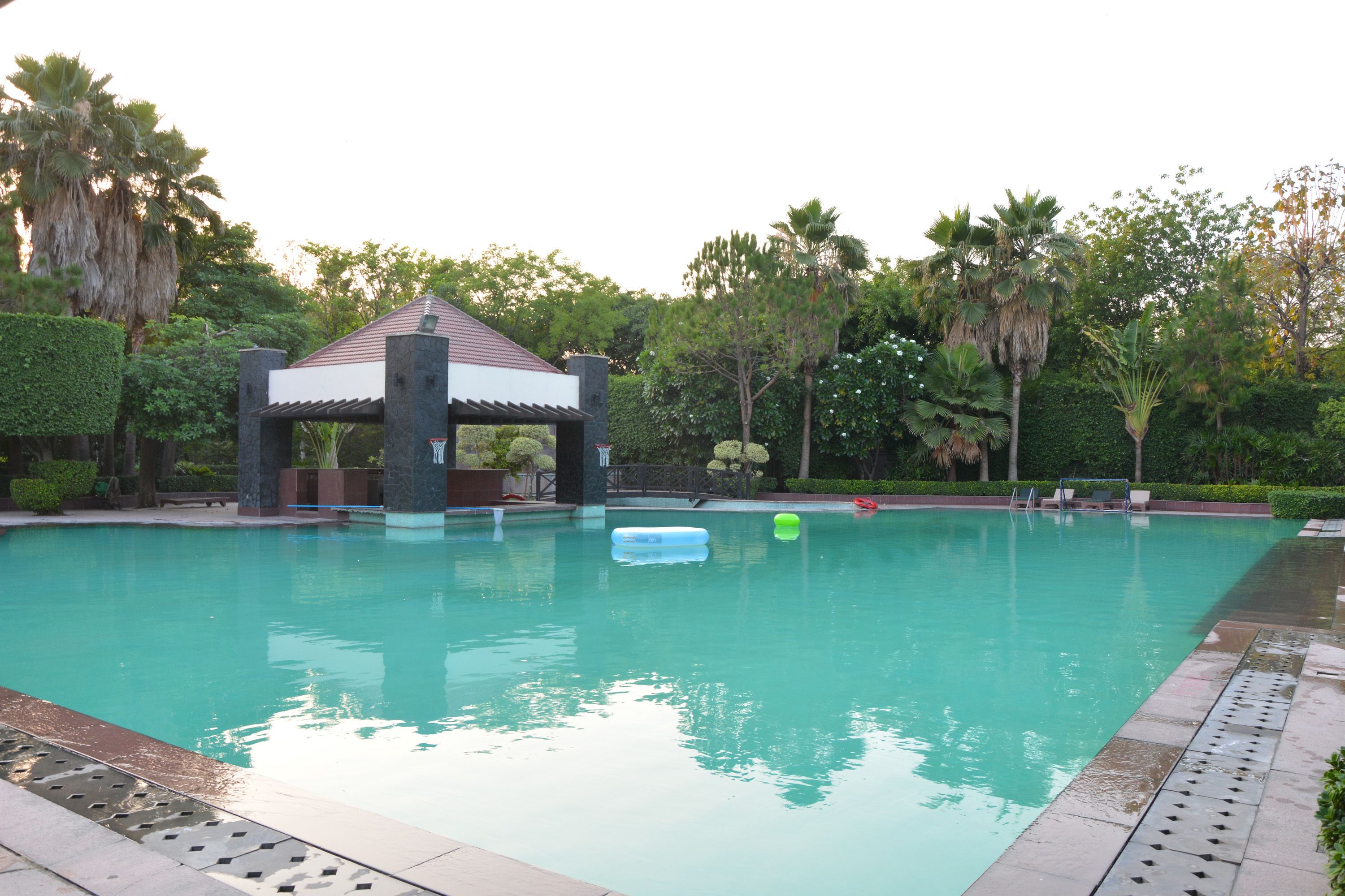 A swimming pool with a gazebo, palm trees, and a clear sky.