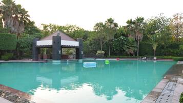 A swimming pool with a gazebo, palm trees, and a clear sky.
