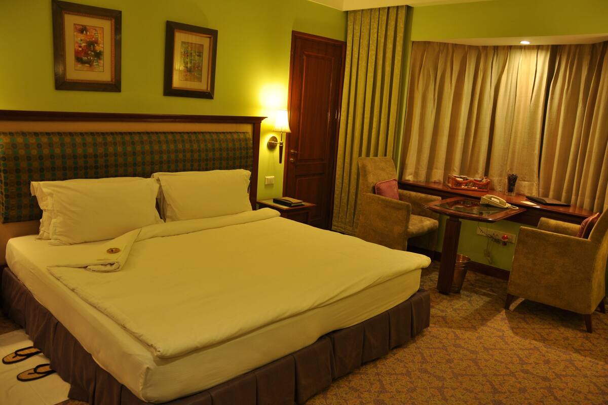 A hotel room with a large bed, a desk with a telephone, and two chairs.