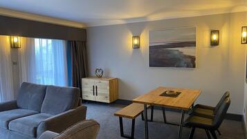 Une chambre d’hôtel moderne avec un canapé gris, une table en bois avec des chaises, un meuble orné d’un motif en forme de cœur et un tableau accroché au mur.