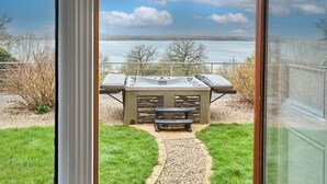 A hot tub with a stone facade, a wooden bench, and a clear view of a lake through a glass door. - Rutland Hall Hotel & Spa (Oakham)