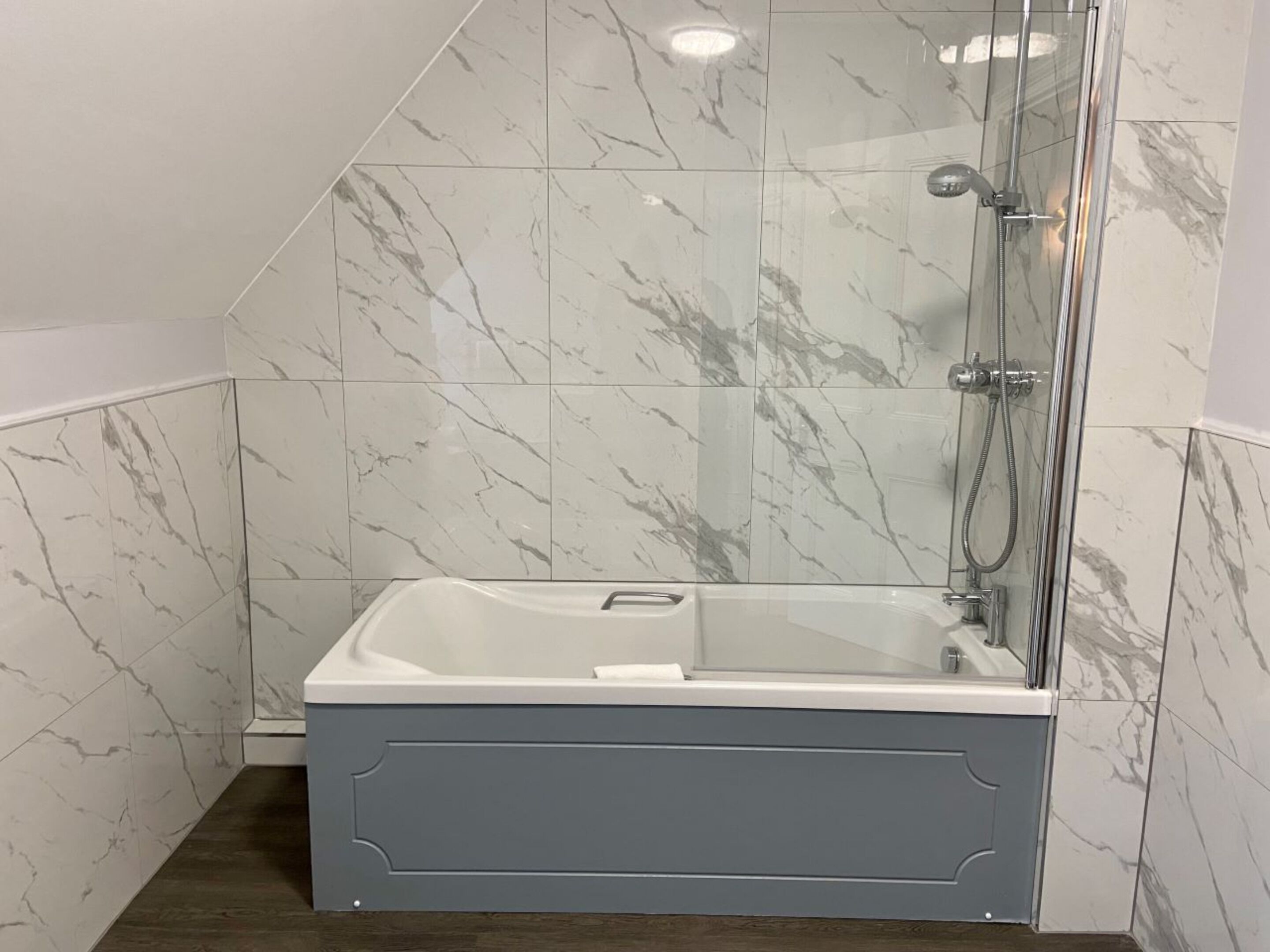 Un baño moderno con ducha de vidrio, baldosas de mármol y una bañera gris.