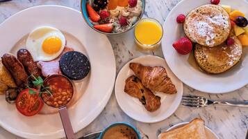 Una mesa con huevos, salchichas, tomates, frijoles y un croissant.