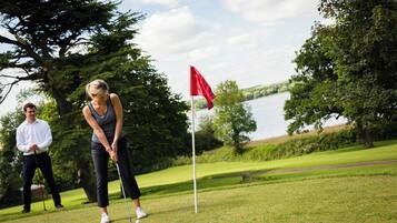 A golf course with a flagstick, a body of water, and trees in the background.
