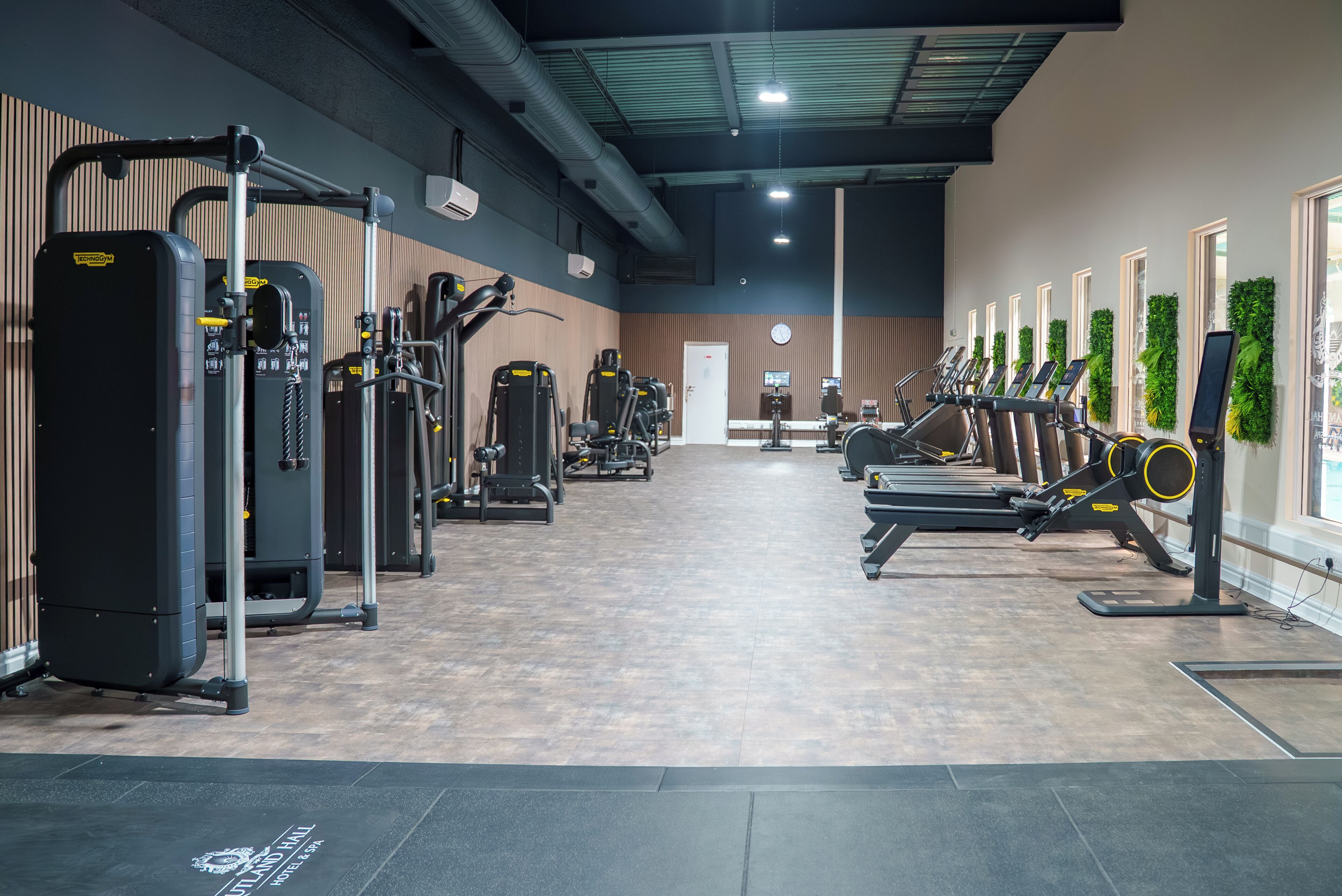 Un gimnasio con varias máquinas de ejercicio, un televisor en la pared y una puerta al fondo.