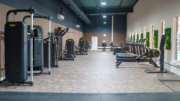 Un gimnasio con varias máquinas de ejercicio, un televisor en la pared y una puerta al fondo.