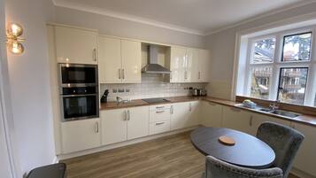 A modern kitchen with white cabinets, stainless steel appliances, a round dining table, and a window with a view of buildings.