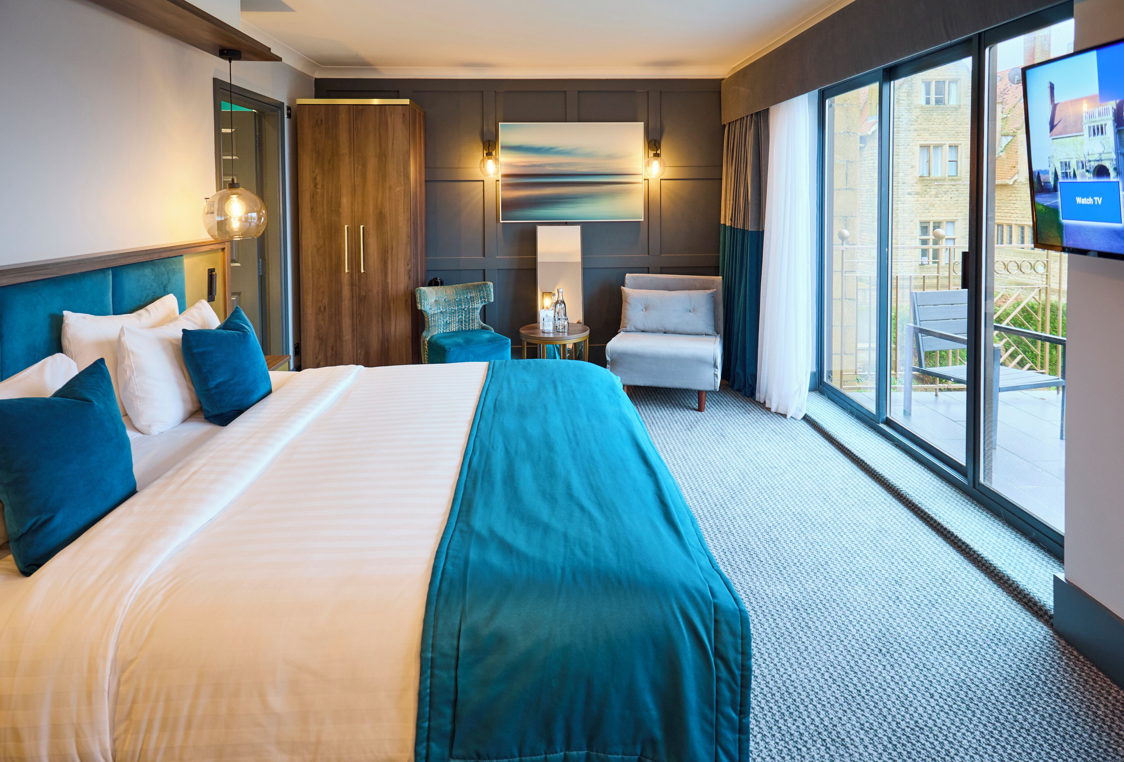 A hotel room with a large bed, a seating area with a table, a TV, and a view of the outside.