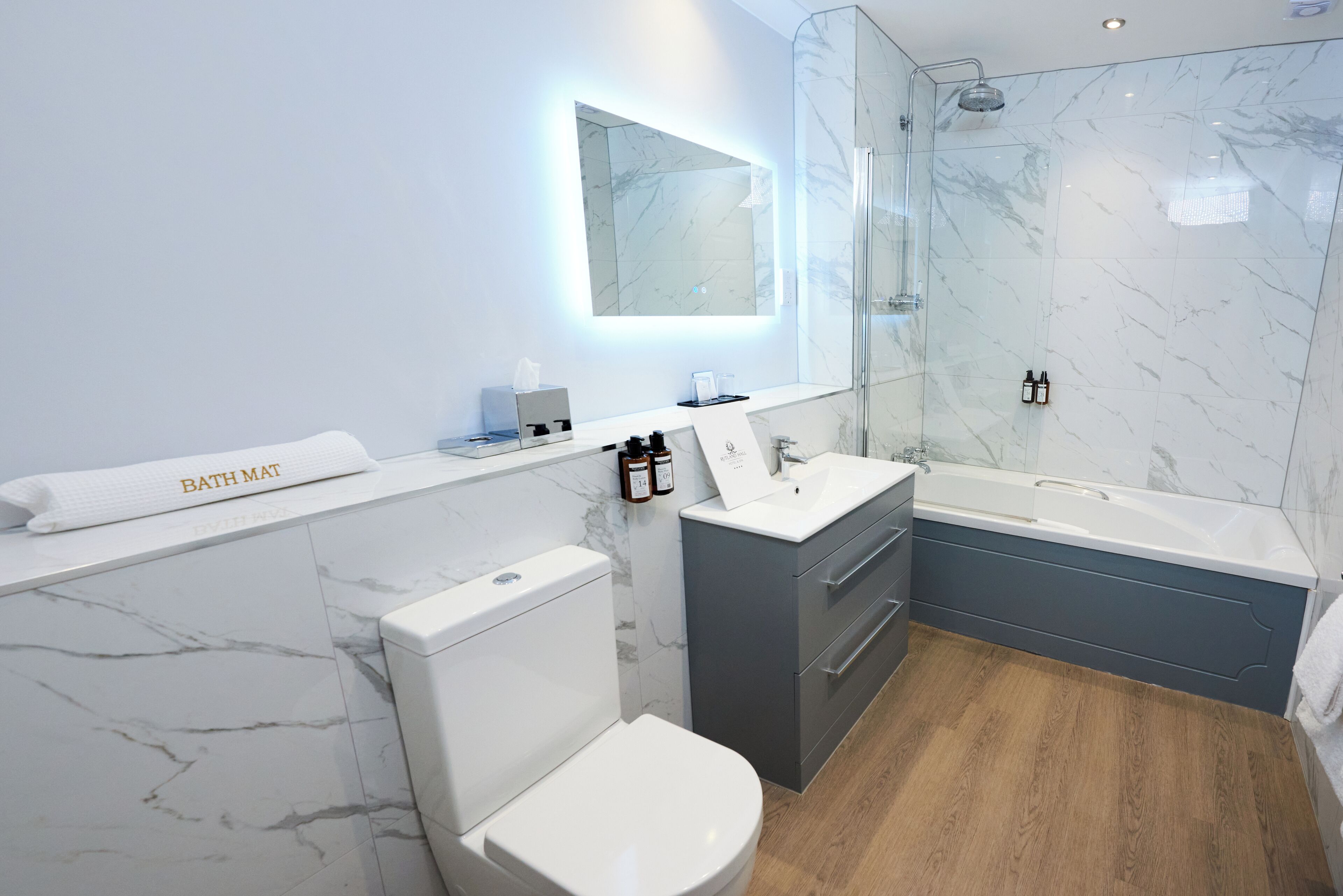 Un baño moderno con pared de mármol, cabina de ducha de vidrio, inodoro blanco, tocador con lavabo y bañera.
