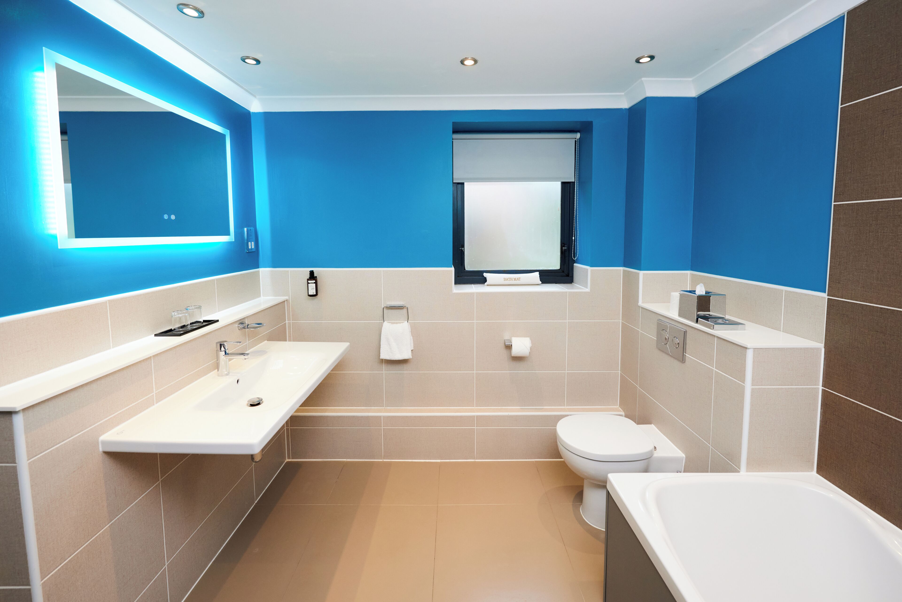 Un baño moderno con un espejo grande, lavamanos, inodoro y bañera.