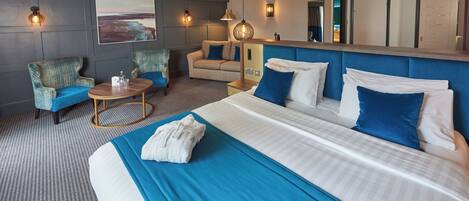 A hotel room with a large bed, a sofa, a chair, a small table, and a mirror.