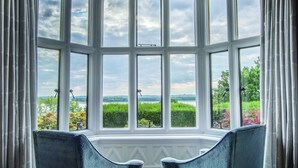 A room with a bay window overlooking a garden and a lake. There are two upholstered chairs and a patterned carpet. - Rutland Hall Hotel & Spa (Oakham)
