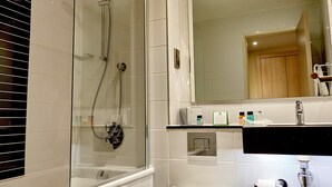 Une salle de bain moderne avec une douche à parois de verre, des toilettes, un lavabo avec un miroir au-dessus et des articles de toilette posés sur le comptoir.